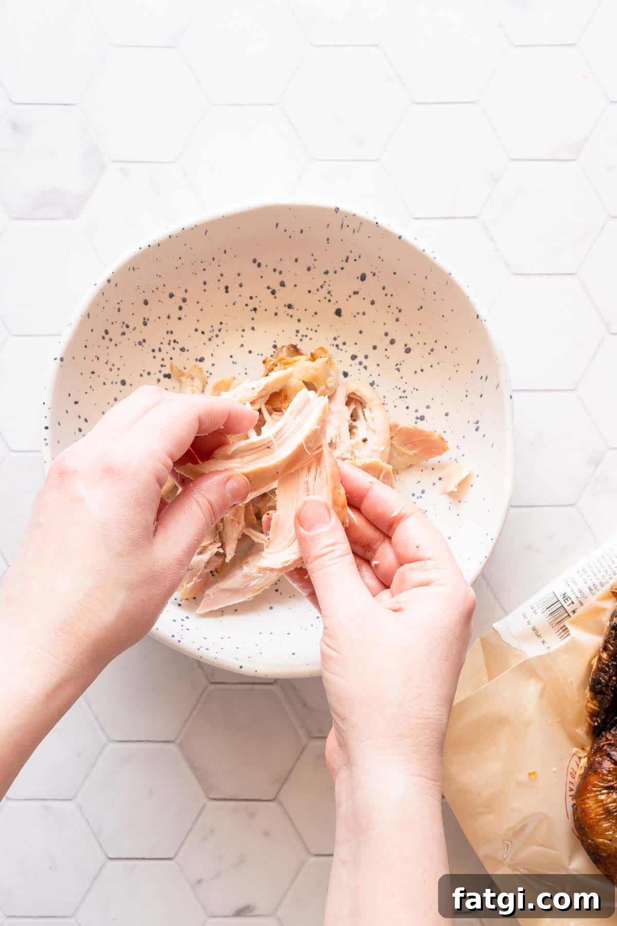 chicken being shredded by hand over a small bowl.
