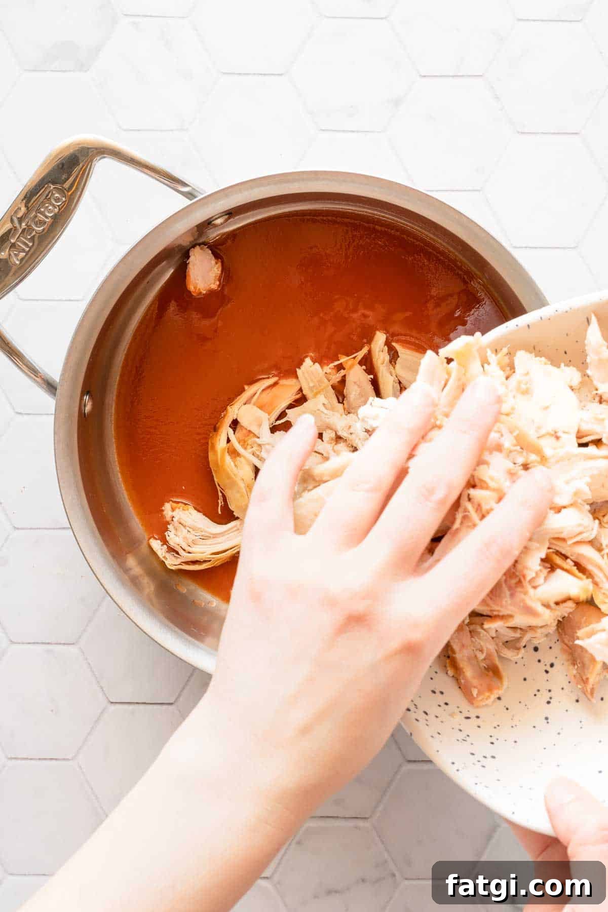 shredded chicken being added into saucepan with hot sauce inside.
